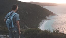 unrecognizable male hiker enjoying seascape from grassy hilltop at sundown